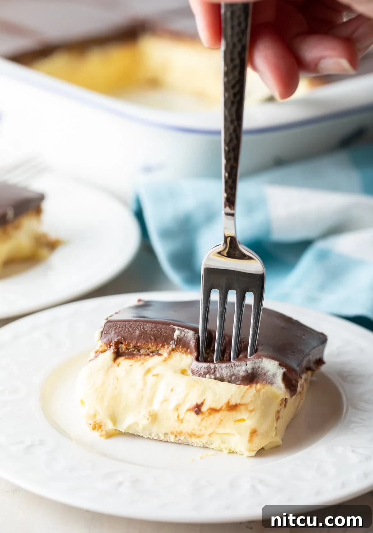 Decadent Chocolate Ganache Eclair Cake 8 A close-up side view of a fork gently entering a slice of the no-bake eclair cake, highlighting the beautiful layers of chocolate ganache, creamy filling, and softened graham cracker, tempting a bite.
