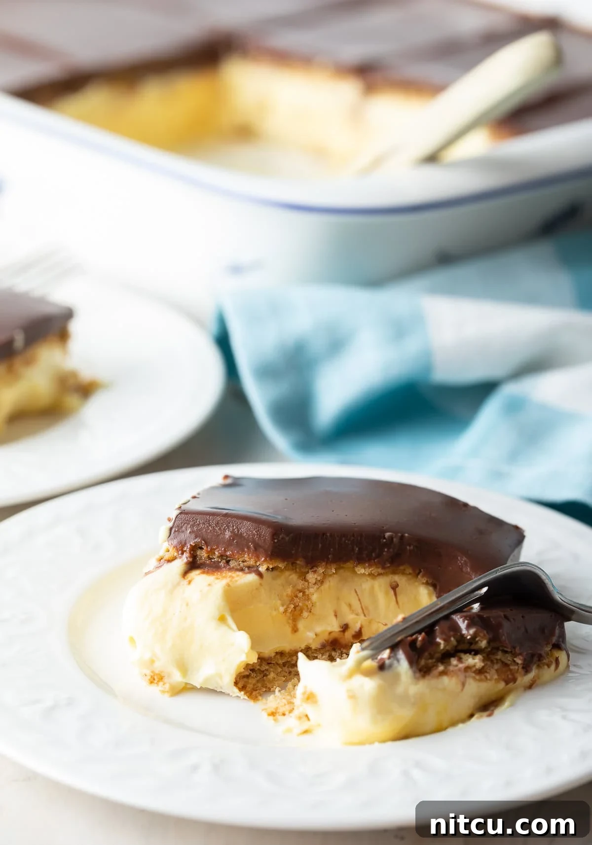 Decadent Chocolate Ganache Eclair Cake 9 A fork lifts a generous slice of the layered no-bake eclair cake from a plate, showcasing the creamy filling and thick chocolate ganache, inviting diners to indulge in its rich texture.