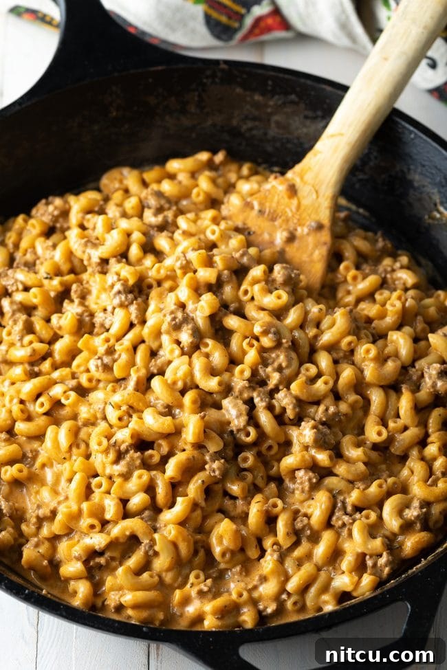 One-Pot Macaroni Stirring A wooden spatula stirring homemade cheeseburger macaroni in a single pot, showcasing the ease of this one-pot meal.