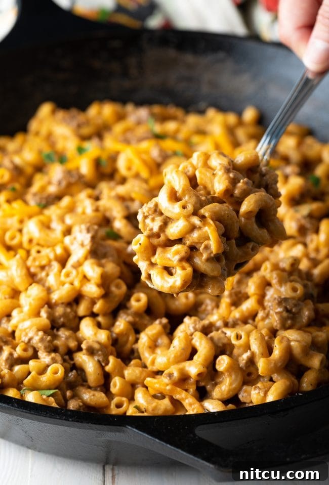 Scooping Cheeseburger Macaroni A serving spoon lifting a portion of cheesy homemade hamburger helper from the skillet, ready to plate.