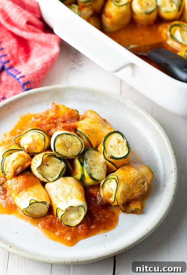 Plated low carb zucchini roll-ups with a generous amount of tomato sauce. 
