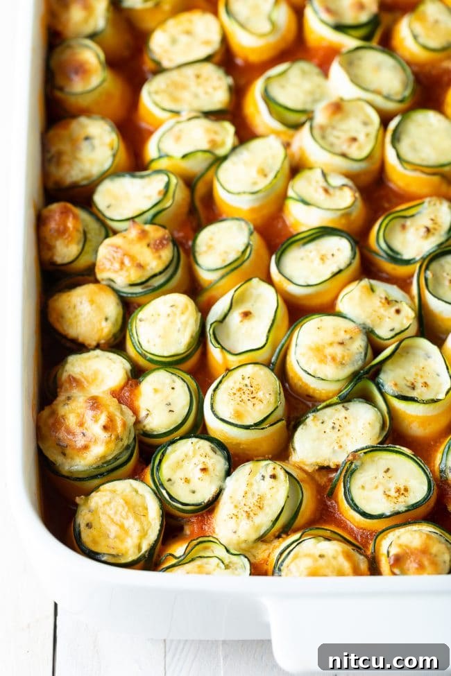 Beautifully baked low carb keto zucchini roll ups presented in a white baking dish.