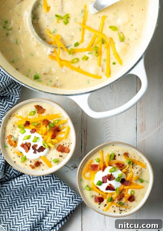 An inviting overhead shot showcasing two bowls of richly garnished loaded potato soup, with a large Dutch oven filled with more soup positioned alongside.