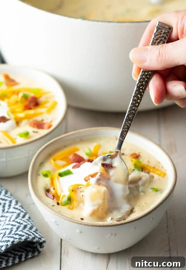 A hand gracefully holds a spoon, preparing to delve into a creamy bowl of potato soup, capturing the anticipation of a warm and comforting bite.