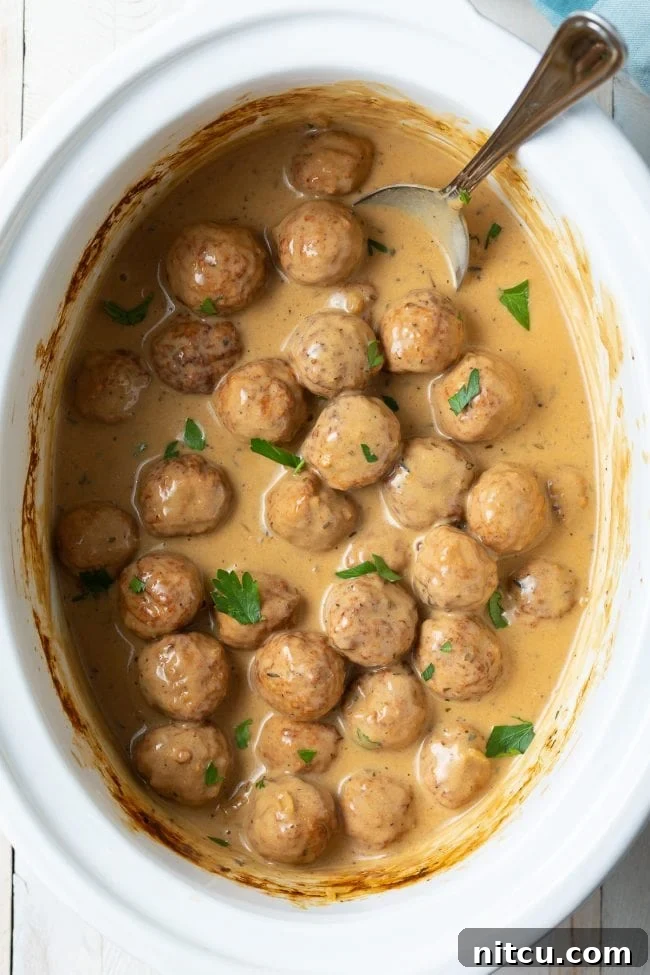 Effortless Slow Cooker Swedish Meatballs 3 Overhead shot of perfectly cooked Swedish Meatballs simmering in their creamy, rich sauce within a slow cooker.