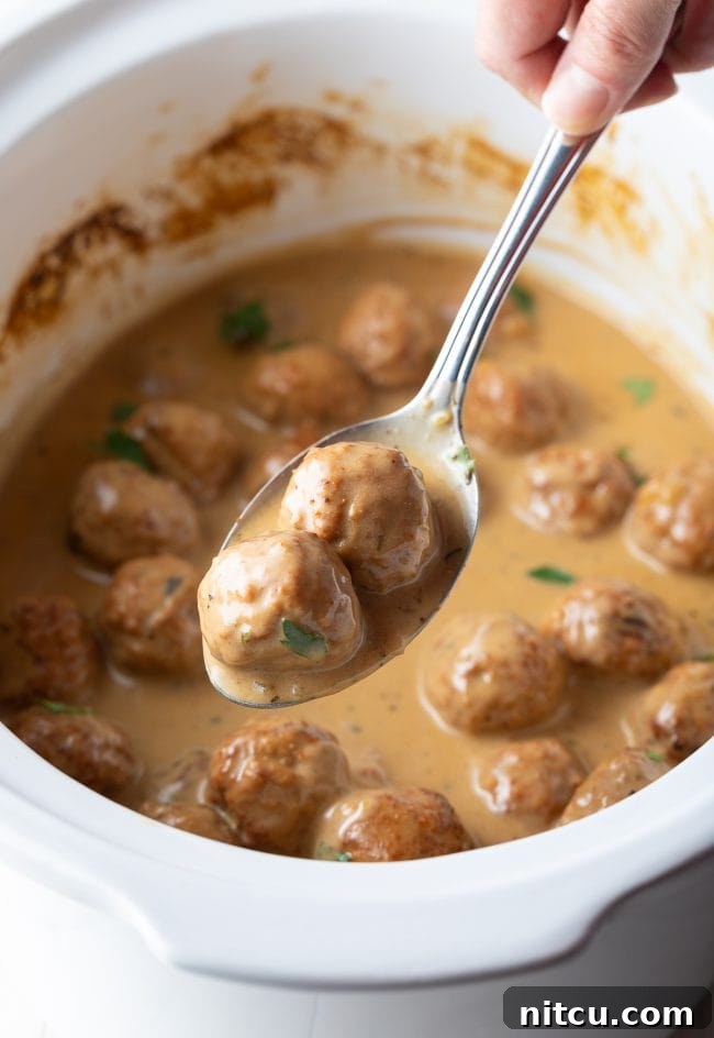 Effortless Slow Cooker Swedish Meatballs 10 A serving spoon lifting a creamy Swedish meatball from the slow cooker, ready to be plated for a delicious meal.