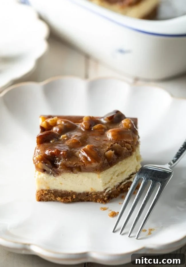Pecan Praline Cheesecake Delight 12 A beautifully presented slice of Pecan Pie Cheesecake with caramel pecan topping on a plate, with a fork beside it, indicating a bite has been taken.