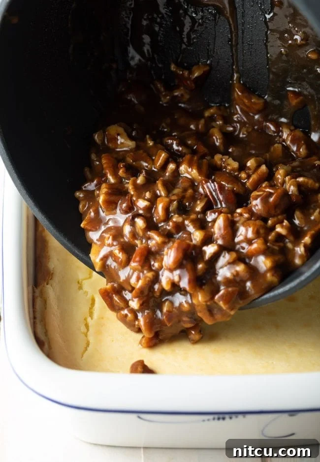 Pecan Praline Cheesecake Delight 9 Gooey pecan caramel topping being carefully poured and spread over the baked cheesecake in a baking dish.