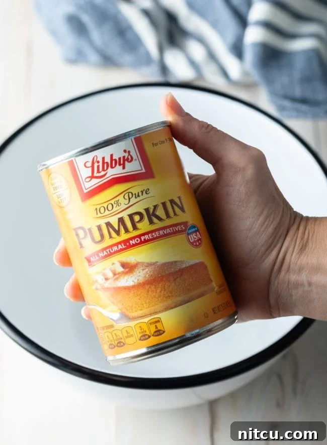 Libbys Classic Pumpkin Pie 5 Hand holding a can of pumpkin over a mixing bowl.