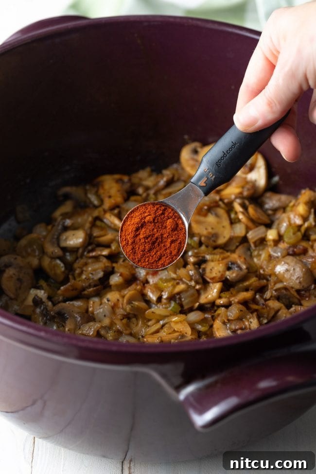 Classic Hungarian Mushroom Soup Made Vegan and Gluten Free 6 A close-up of smoked paprika being added to sautéed mushrooms and onions in a pot.