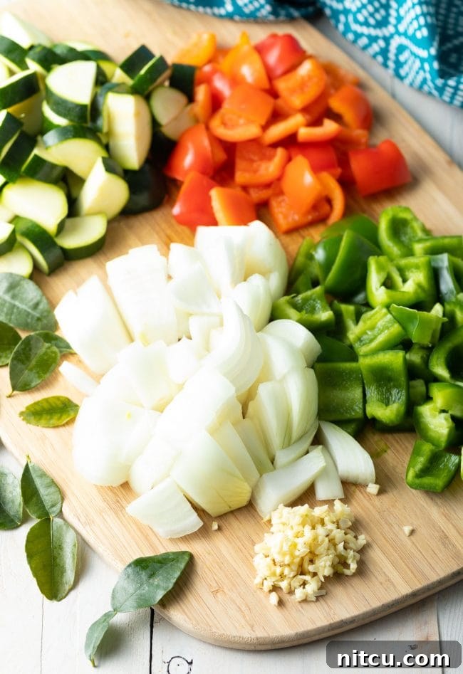 Effortless Instant Pot Thai Green Curry 5 Freshly chopped bell peppers, onions, and zucchini on a cutting board, ready for the Instant Pot.