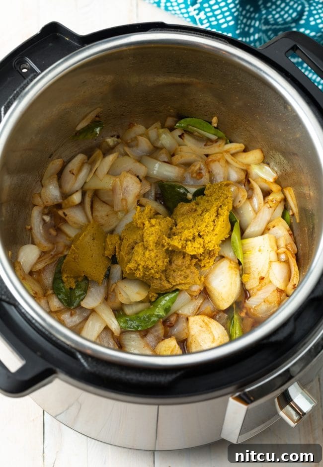 Effortless Instant Pot Thai Green Curry 6 Overhead shot of onions, garlic, and kaffir lime leaves sautéing in the Instant Pot with green curry paste.