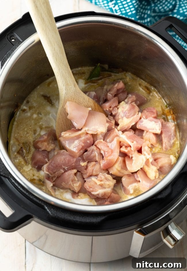Effortless Instant Pot Thai Green Curry 7 Diced chicken pieces being added to the Instant Pot, ready to be coated in the curry base.