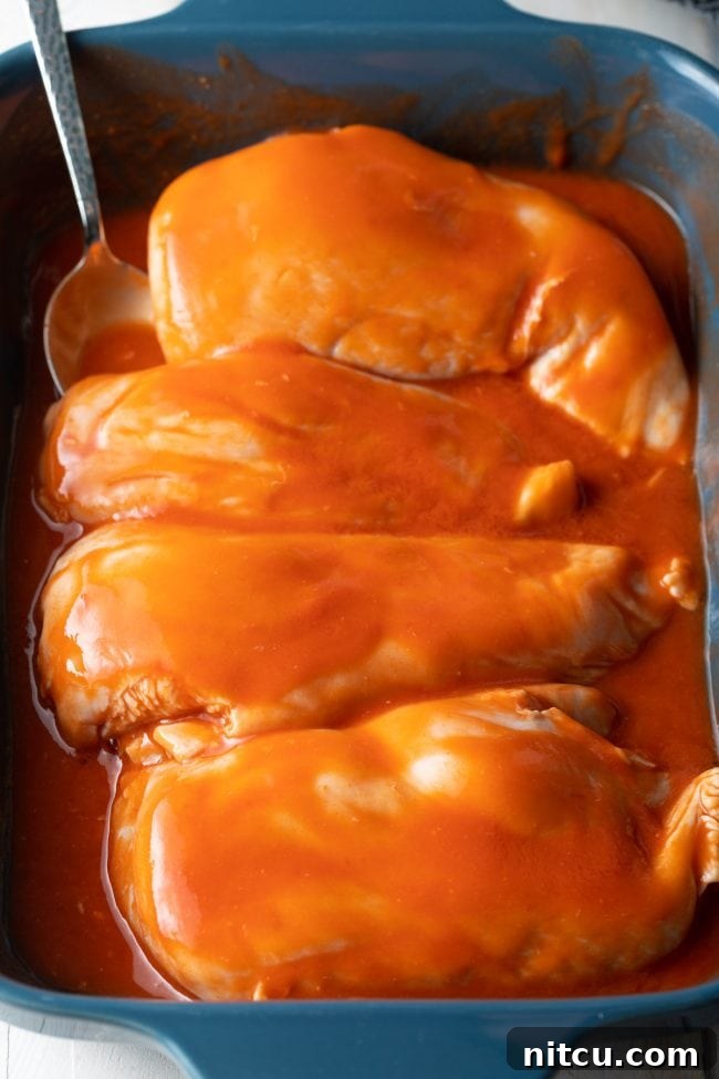Boneless chicken breasts soaking in a vibrant cayenne pepper sauce within a baking dish, ready for marination.