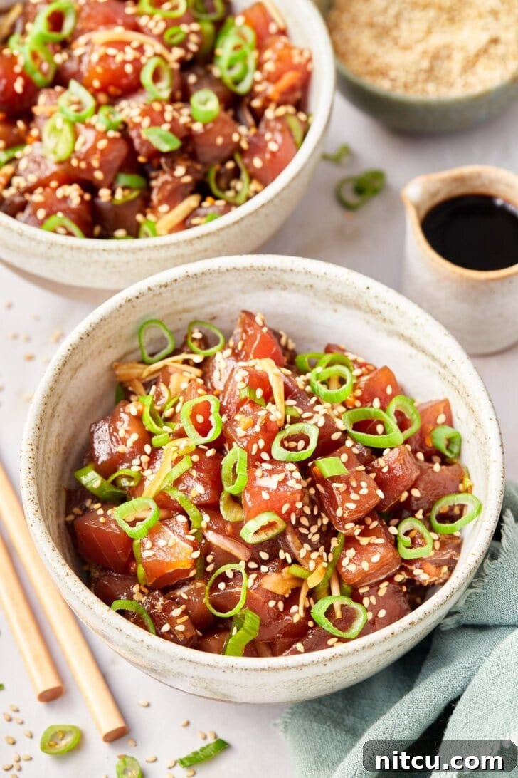Two vibrant bowls filled with fresh Ahi Poke, garnished with green onions and sesame seeds, ready to be enjoyed with a side of soy sauce.