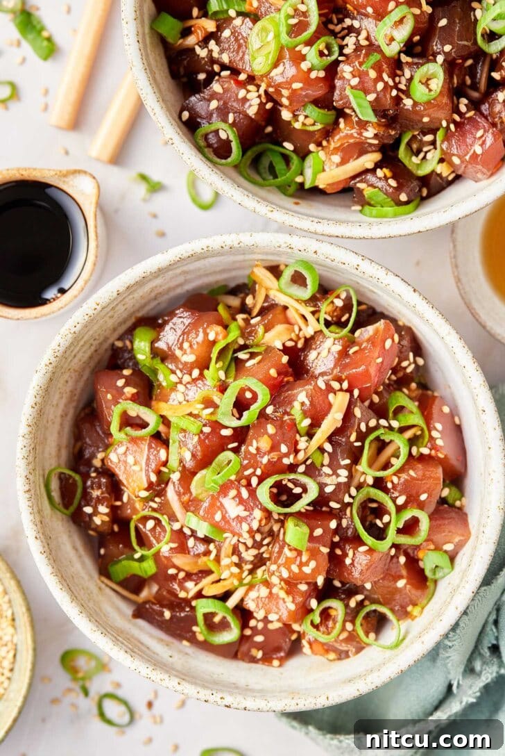 A beautifully plated bowl of tuna poke, generously topped with thinly sliced scallions and a sprinkle of sesame seeds, highlighting its fresh appeal.