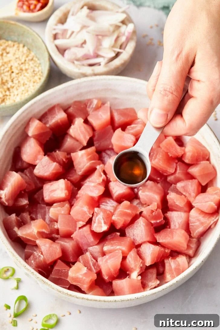 Sauce being poured over perfectly chopped tuna, preparing for a delicious Ahi Poke.