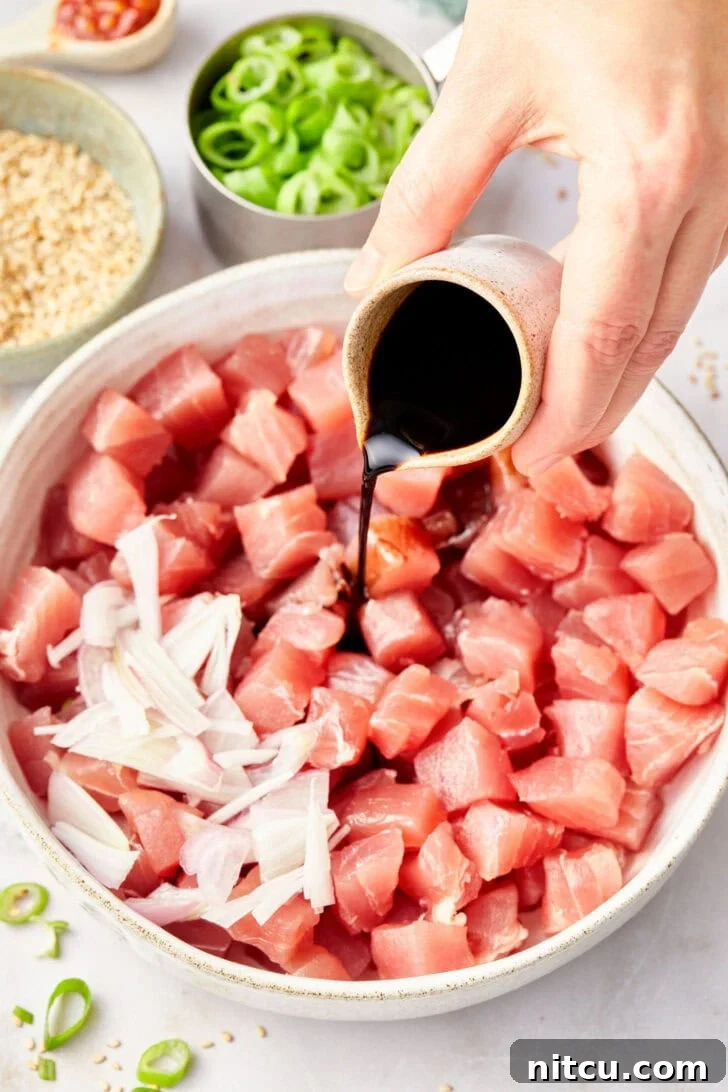 Tuna cubes topped with freshly sliced shallots and a rich marinade, ready for mixing to create Ahi Poke.