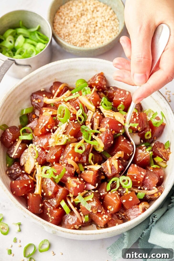 A spoon gently mixing ingredients for Ahi Poke, ensuring every piece of tuna is perfectly coated with the flavorful sauce.