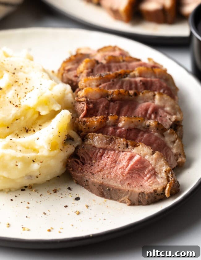 sliced duck breast with mashed potatoes on a white plate