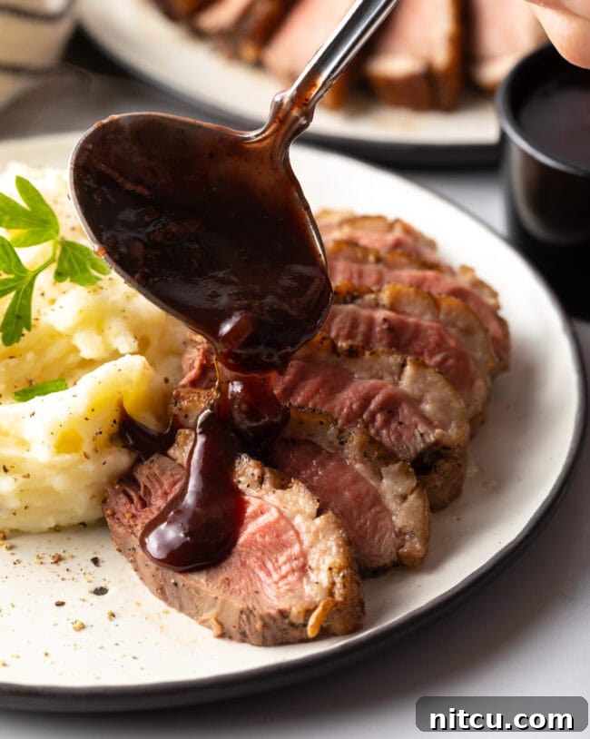 how to pan sear duck breast - shown on plate sliced and drizzled in sauce