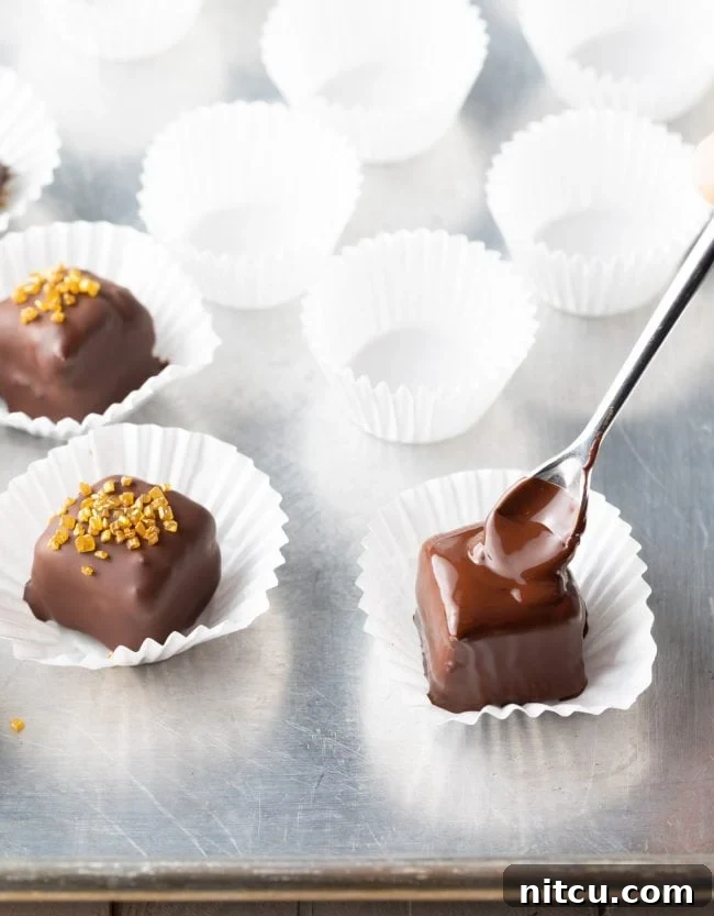 A mini cake being expertly coated in melted chocolate, showing the smooth, even coverage.
