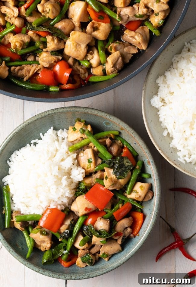 An overhead shot of homemade Thai Basil Chicken with rice, served in a pan and individual bowls.
