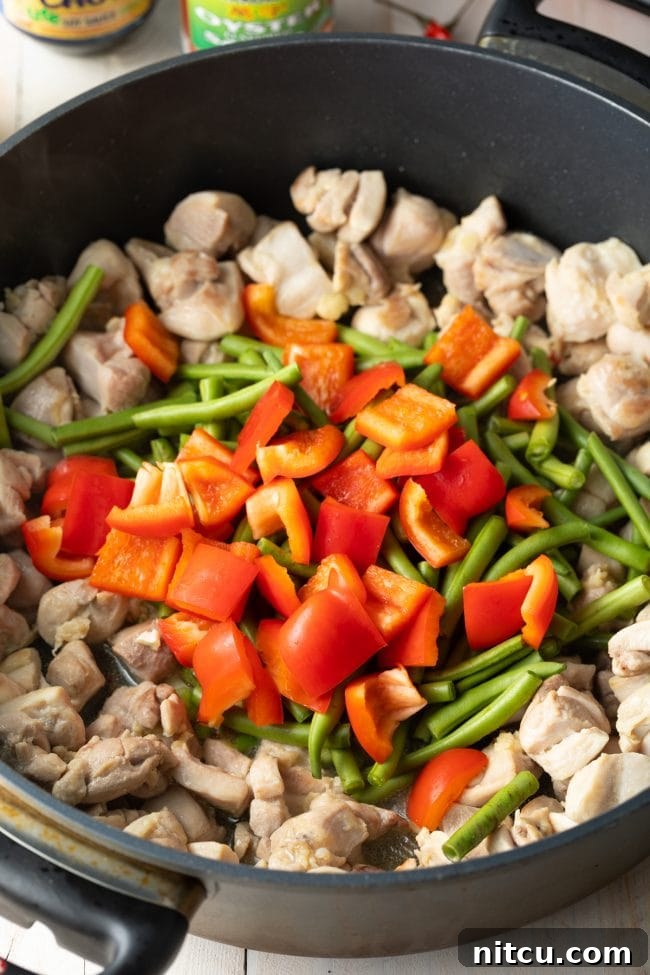 Chicken and various vegetables cooking in a large skillet, stir-frying process shot.