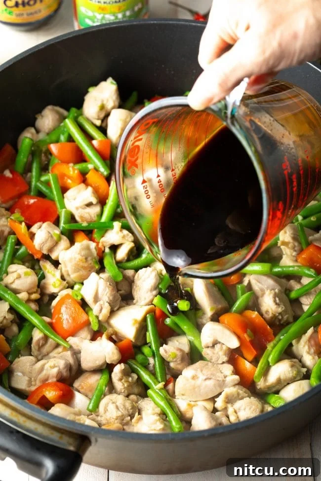 Pouring the savory sauce into the chicken and vegetable stir-fry in a pan.