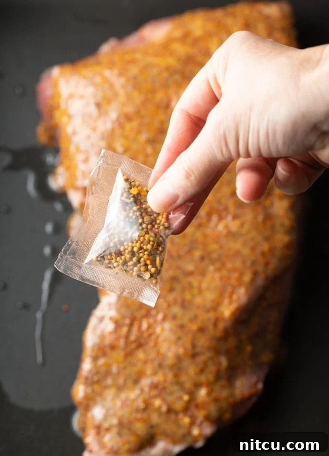 Hand holding the packed of corned beef seasoning above the raw corned beef brisket. 