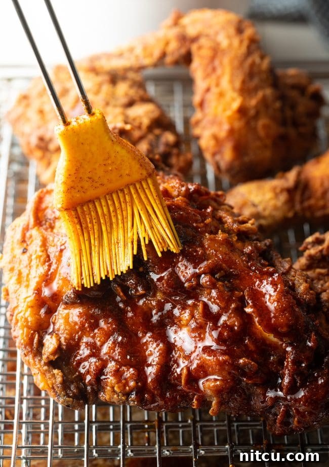 Nashville Hot Chicken 12 A brush applying vibrant red spicy oil evenly over the surface of a fried chicken piece.