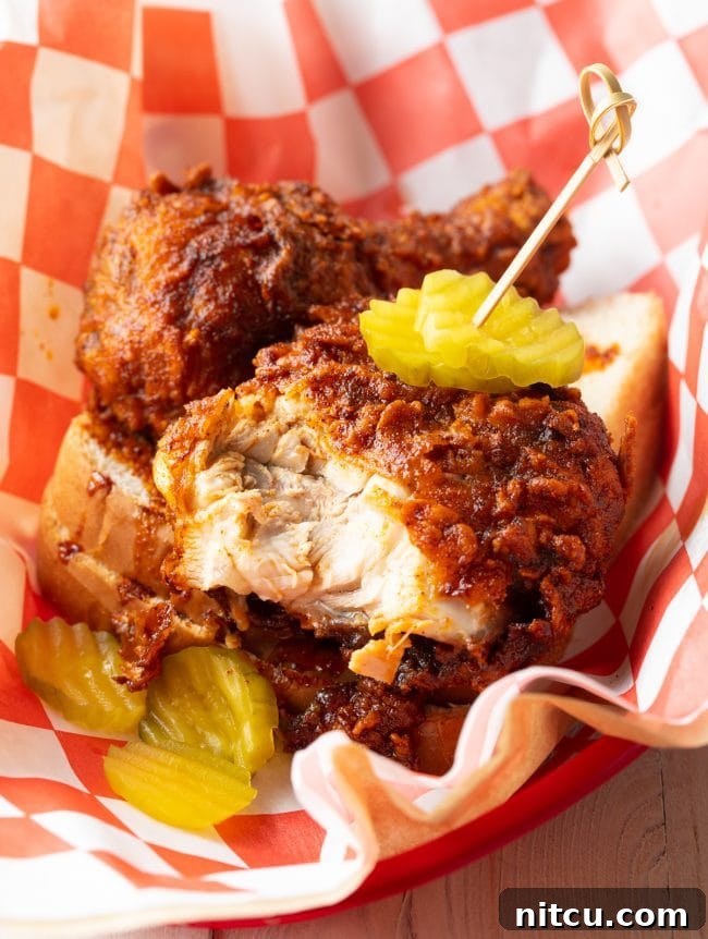 Nashville Hot Chicken 4 A piece of Nashville hot chicken, sliced open to reveal its tender, juicy breast meat, resting in a serving basket alongside fresh dill pickles.