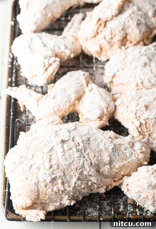 Nashville Hot Chicken 7 Breaded chicken pieces resting on a wire rack, allowing the coating to adhere properly before frying.