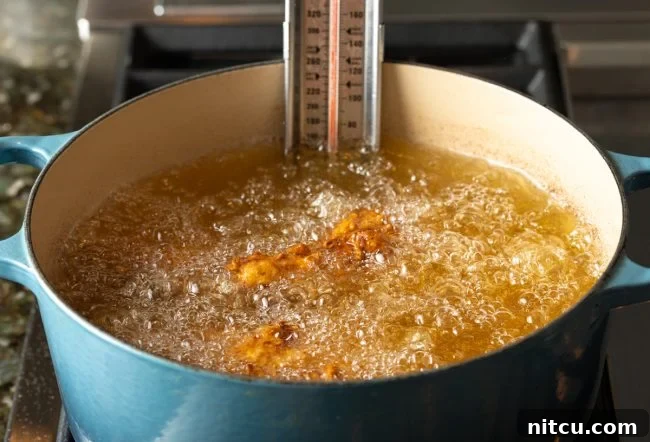 Nashville Hot Chicken 8 Several pieces of chicken sizzling and frying in a pot of hot oil, turning golden brown.