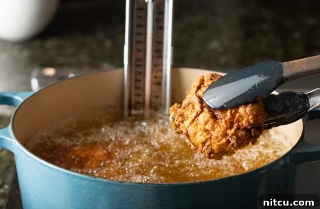 Nashville Hot Chicken 9 Golden-brown fried chicken being carefully lifted out of hot oil with tongs, showcasing its crispy texture.