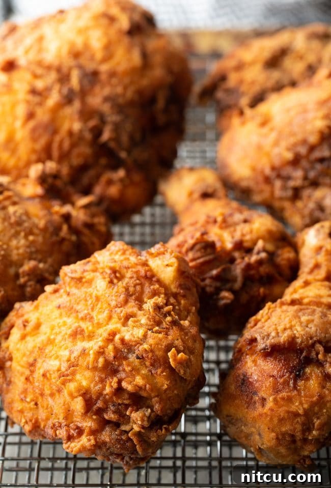 Nashville Hot Chicken 10 Freshly fried chicken pieces resting on a wire rack, allowing excess oil to drain and maintain crispness.