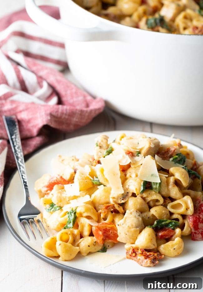 Luscious Tuscan Chicken Pasta 4 White plate of creamy tuscan chicken pasta with a fork on the side.