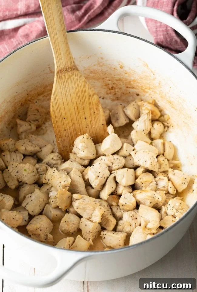 Luscious Tuscan Chicken Pasta 5 Sautéing chunks of chicken in a white dutch oven with a wood spatula.