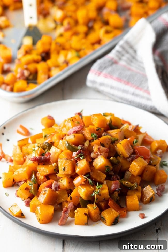 Sweet Potato and Bell Pepper Hash 2 Sweet potato hash browns served on a white plate, with a baking sheet filled with more hash browns visible in the background, showcasing their golden-brown texture.