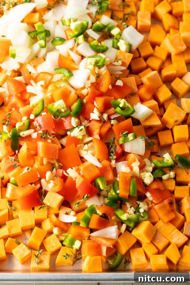 Sweet Potato and Bell Pepper Hash 4 A large baking sheet filled with an array of vibrant, freshly chopped vegetables including sweet potatoes, bell peppers, onions, and jalapeños, ready for roasting.