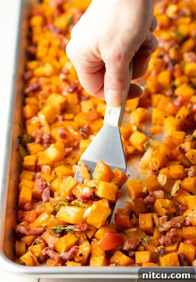 Sweet Potato and Bell Pepper Hash 5 A spatula gently flipping the mixture of sweet potatoes and other vegetables on a baking sheet, ensuring even cooking and browning.
