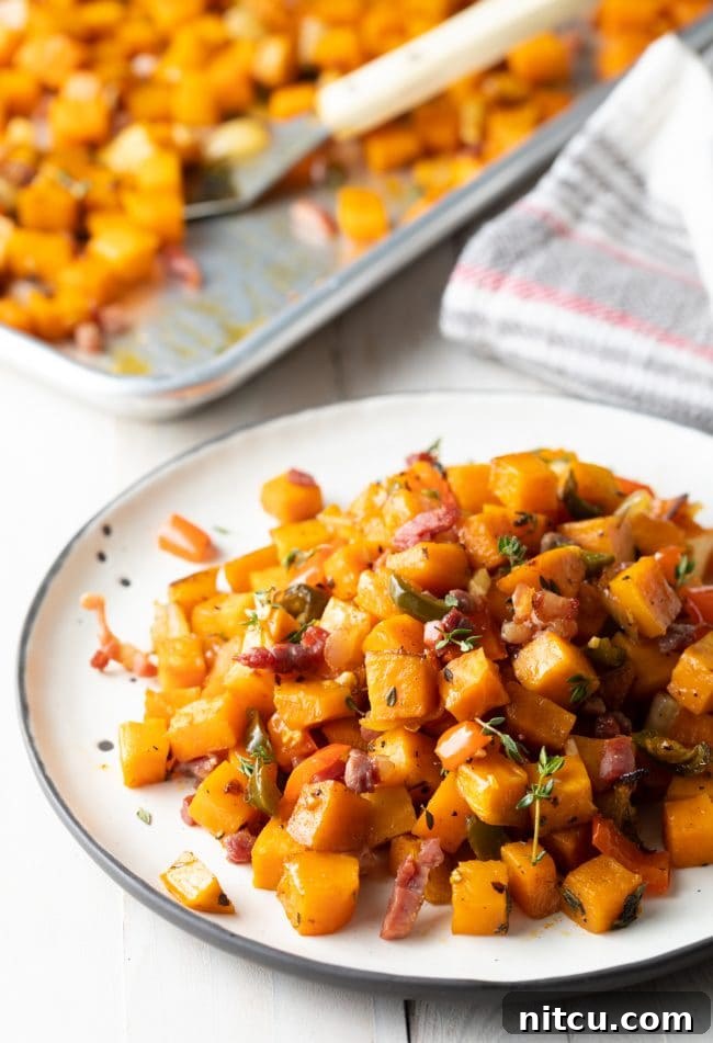 Sweet Potato and Bell Pepper Hash 8 A white plate holding a generous serving of sweet potato hash browns, with a blurred background showing a baking sheet full of the same delicious dish.