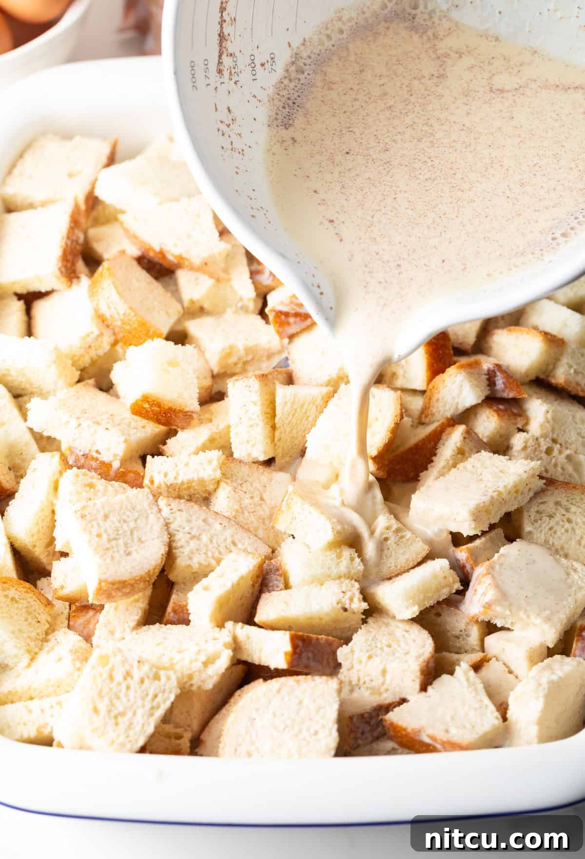 An egg and cream mixture is being poured over slices of bread for overnight French toast casserole.