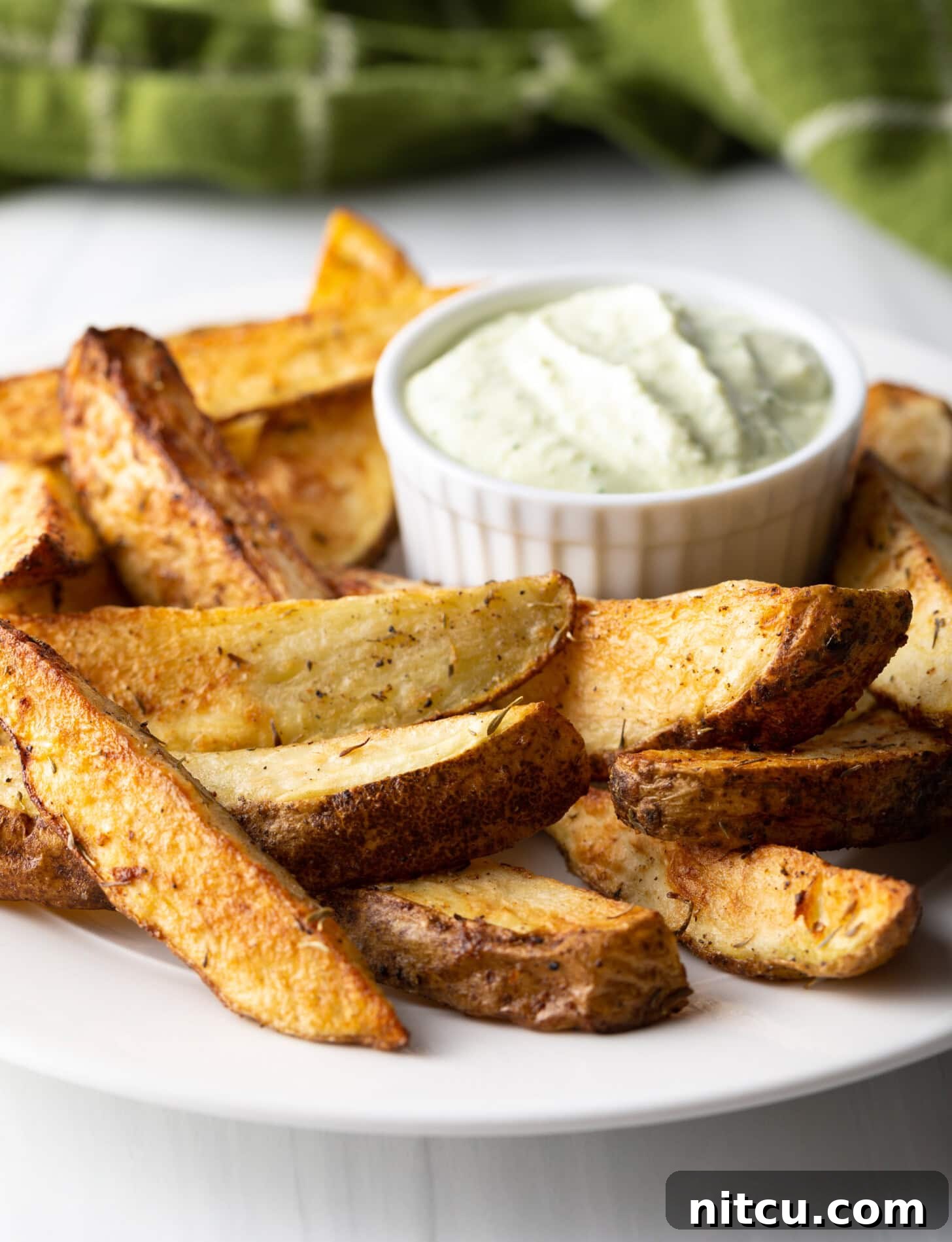 Crispy Golden Air Fryer Potato Wedges 13 A beautiful side view of a white plate generously filled with thick-cut potato wedges, perfectly cooked in an air fryer, with a small white ramekin of dipping sauce alongside.