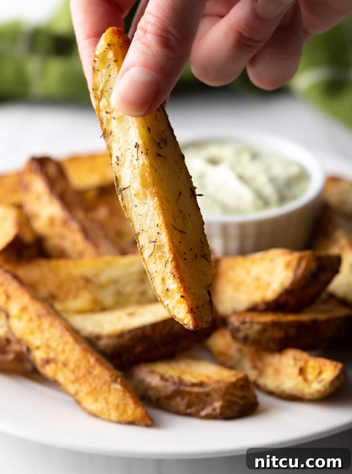 Crispy Golden Air Fryer Potato Wedges 5 A single, perfectly golden-brown air fryer potato wedge is held delicately in a hand, showcasing its crispy exterior.
