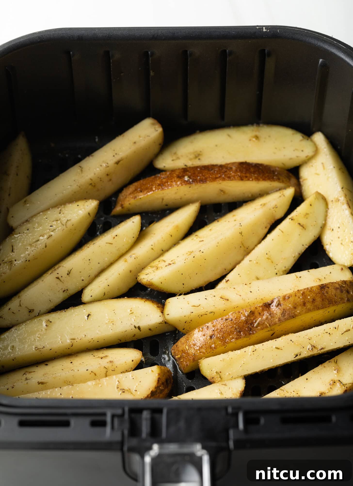 Crispy Golden Air Fryer Potato Wedges 9 Raw potato wedges, cut into thick slices, are carefully spread in a single, even layer within the black basket of an air fryer, ready for cooking.