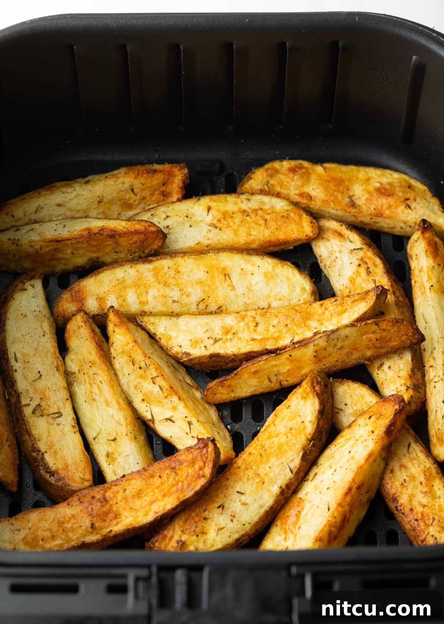 Crispy Golden Air Fryer Potato Wedges 10 A close-up view of beautifully crispy, golden-brown air-fried potato wedges nestled in a black air fryer basket, steam gently rising.