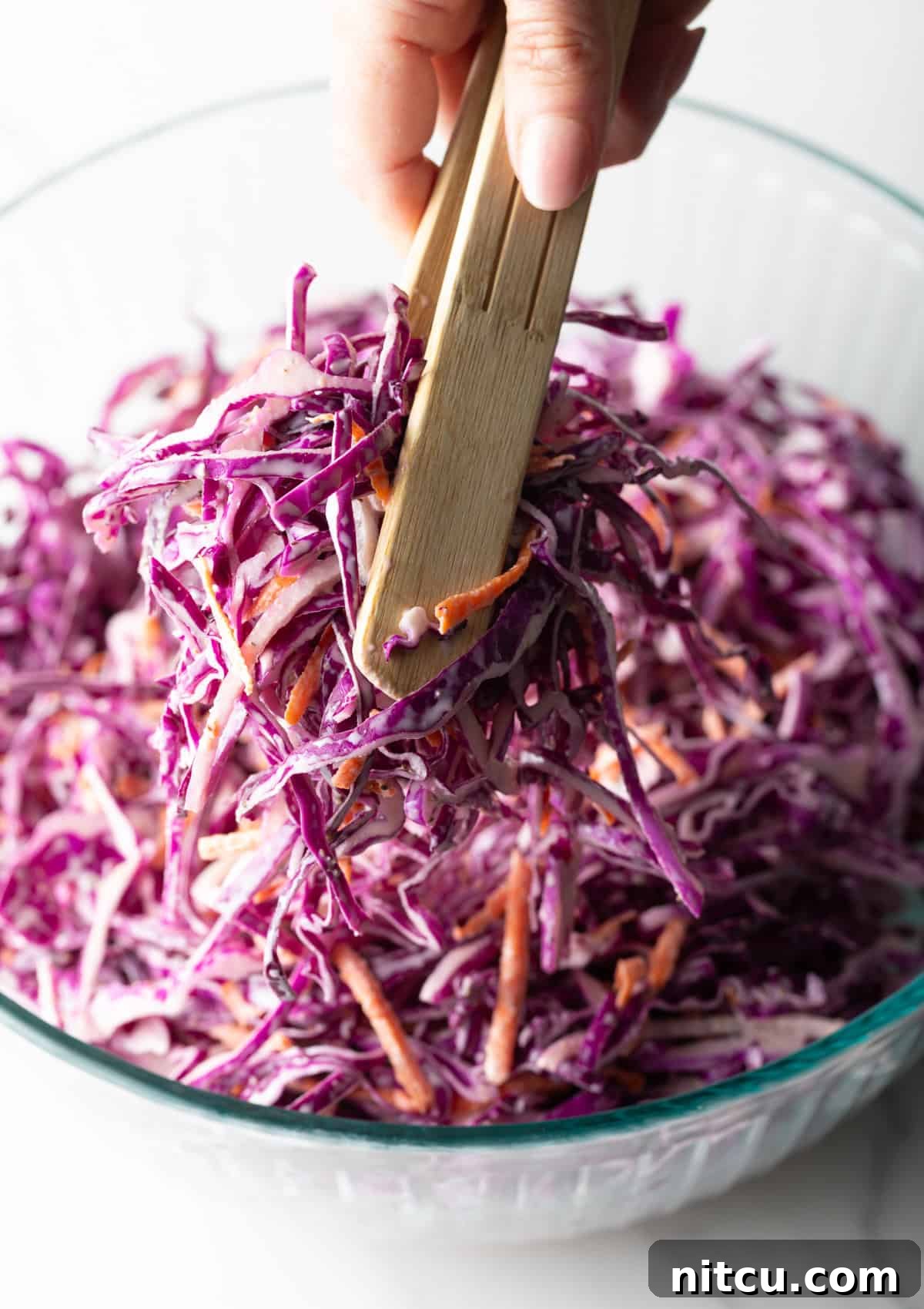 Crimson Cabbage Crunch 8 Red cabbage slaw is being tossed with wooden tongs in a glass bowl.