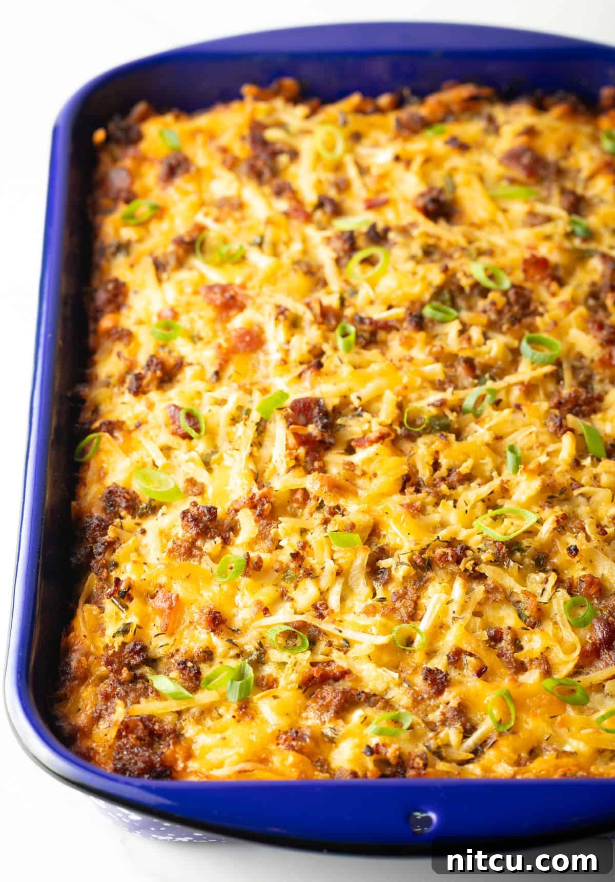 Golden Hash Brown Breakfast Bake 11 A freshly baked breakfast casserole with hash browns, boasting a golden-brown and bubbly top, rests invitingly in a blue baking dish.