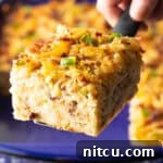 A slice of hashbrown breakfast casserole is being held by a metal spatula above a blue baking dish, ready to be served.